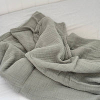 Folded sage muslin fabric on a white surface