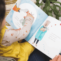 Person reading a children's book with illustrated pages and a child's arm visible.
