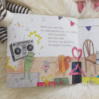 Illustrated book page with a frog, squirrel, and mouse celebrating, surrounded by balloons and music notes.