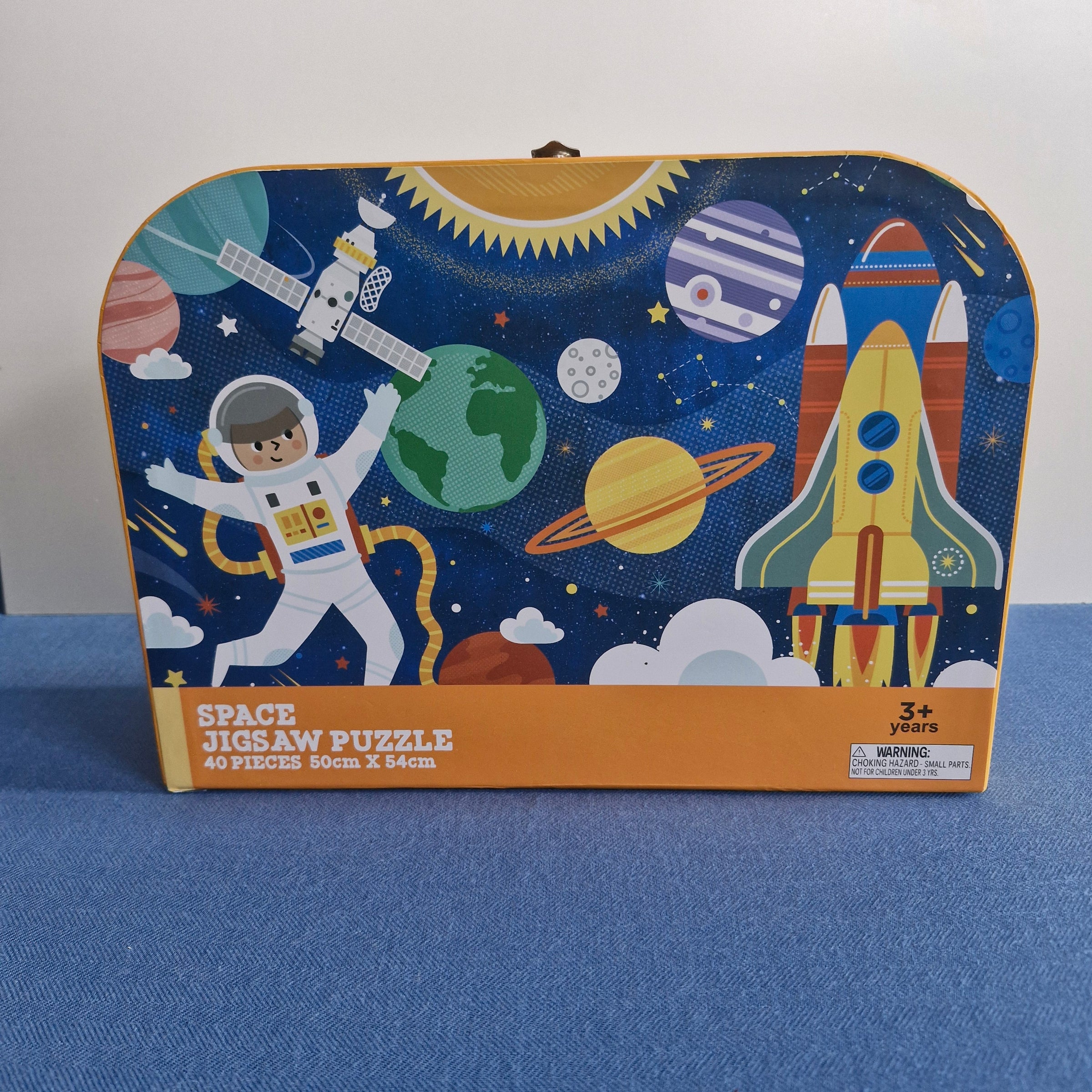 Space-themed jigsaw puzzle box with astronauts, planets, and rockets on a blue background.