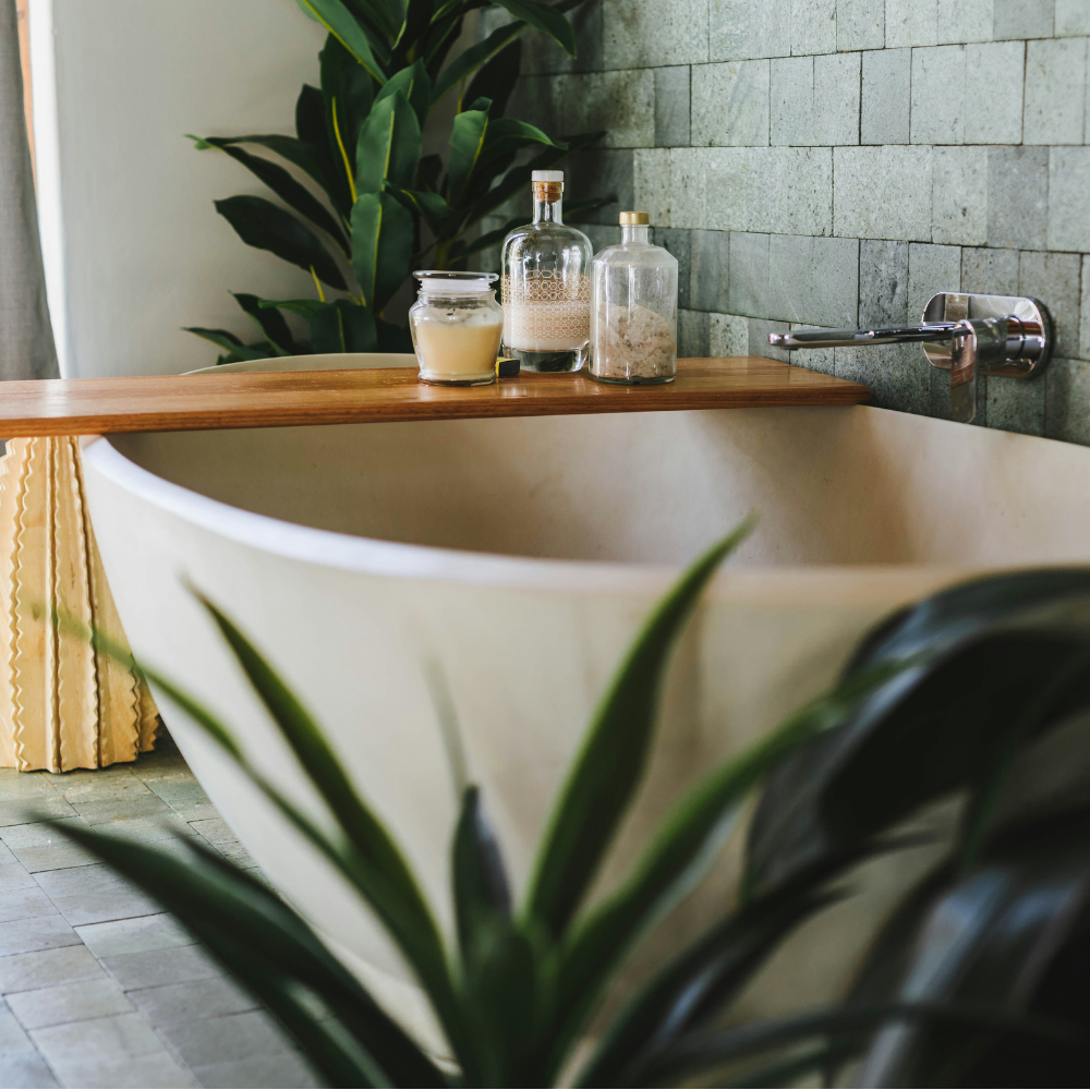 Stone bath with wooden over bath caddy holding glass bottles of salts 