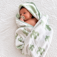Baby wrapped in hooded cotton bath towel with sage green and white cactus pattern laying on white patterned background