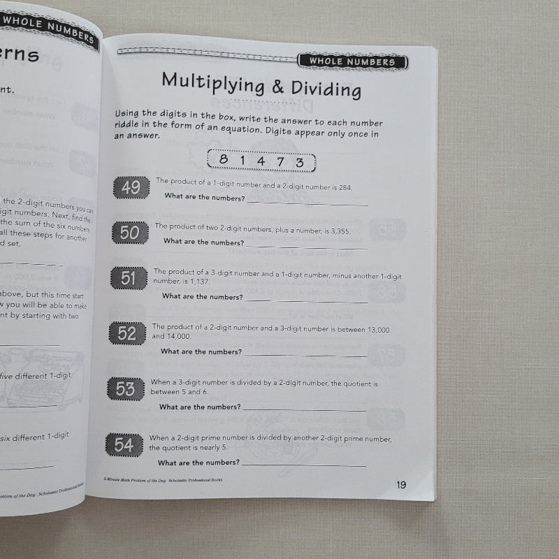 Open math workbook page on multiplying and dividing whole numbers with a gray background