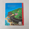 Back book cover with a scenic illustration of a coastal road and houses, on a textured grey background.