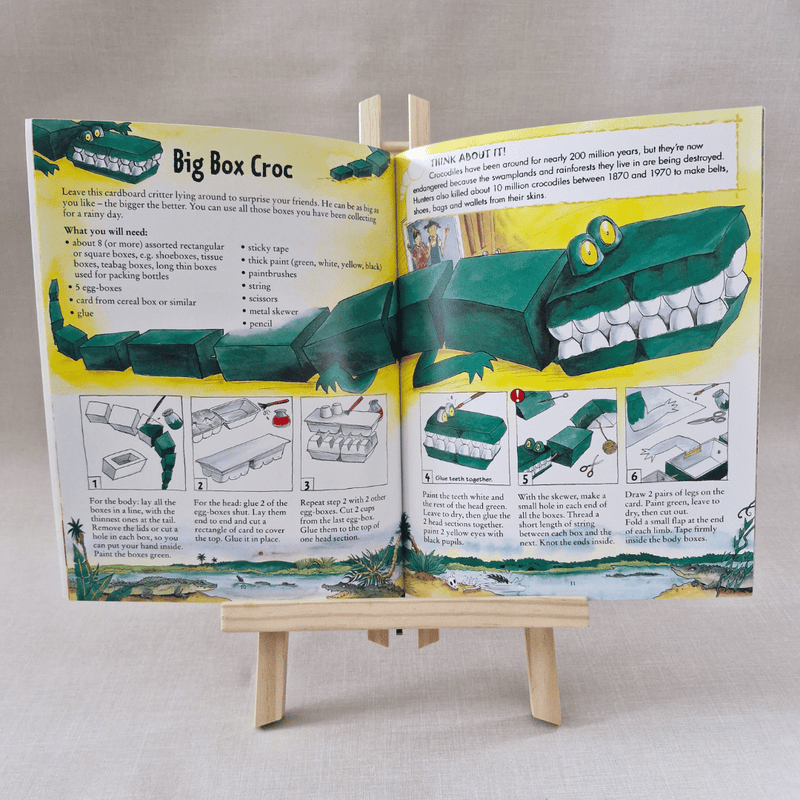 Open book with instructions on creating a cardboard crocodile model, displayed on a small wooden easel.
