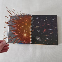 Atlas of space book with galaxy design on clear sheet held by a hand against a light gray background