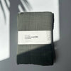 Folded sage green muslin swaddle blanket with a label on a light grey background
