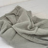 Folded sage muslin fabric on a white surface