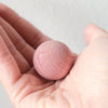 Hand holding a wooden cedar moth ball against a light grey background