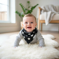 Baby wearing a star-patterned bib on a white rug in a bright room.