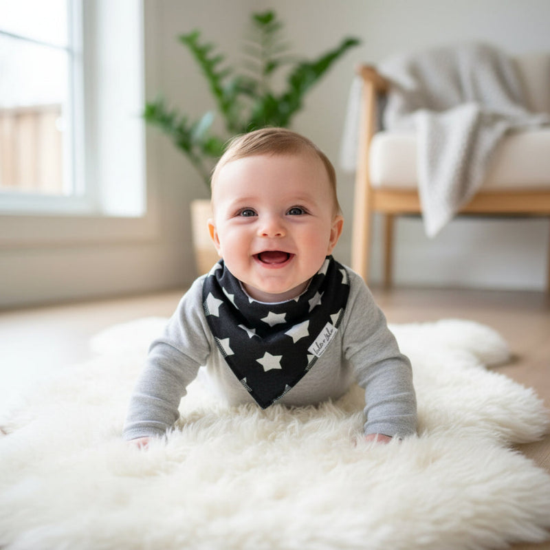 Baby wearing a star-patterned bib on a white rug in a bright room.