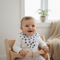 Baby sitting in a wooden chair wearing a star-patterned bib, smiling.