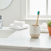 Bamboo toothbrush sitting in ceramic cup on a vanity top