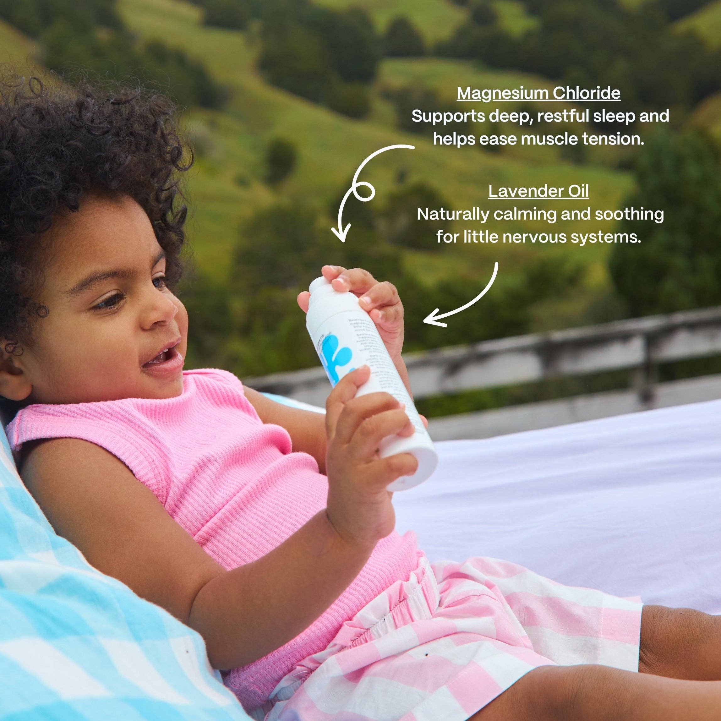 Child holding a bottle with text about magnesium chloride and lavender oil, outdoors.