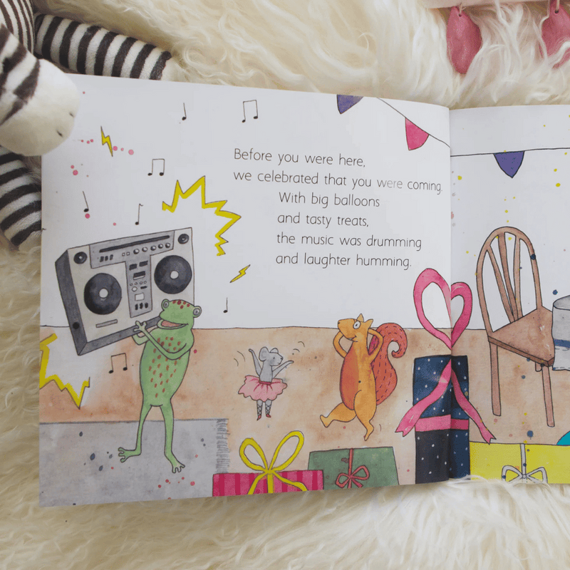 Illustrated book page with a frog, squirrel, and mouse celebrating, surrounded by balloons and music notes.