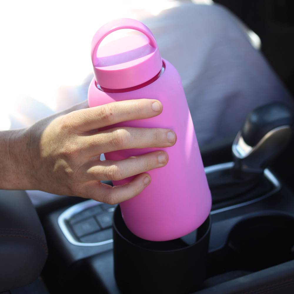 Pink water bottle held by a hand inside a car.