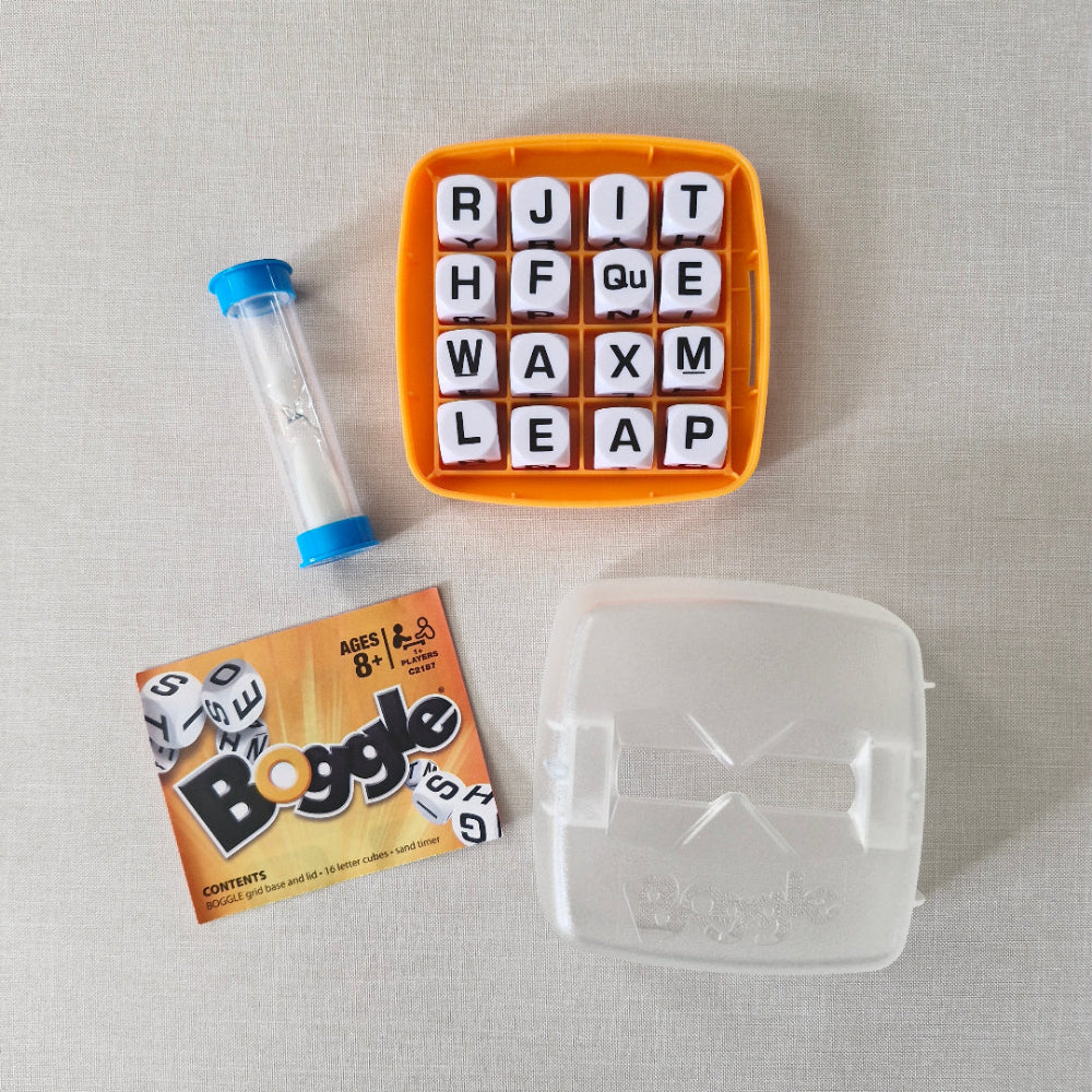 Boggle game components including letter tiles and a sand timer tube on a light grey background.