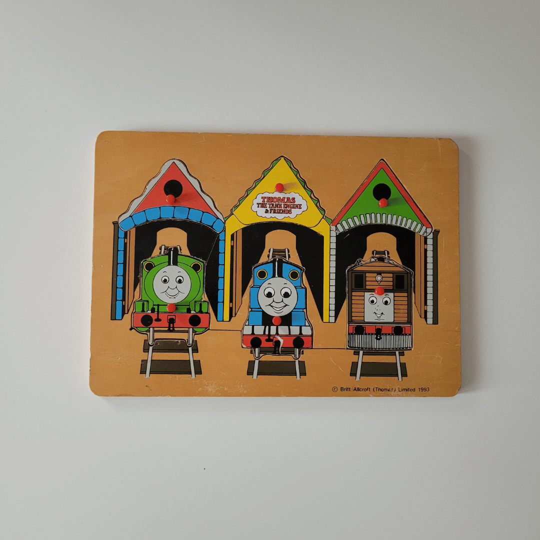 Vintage 'Thomas the Tank Engine' toy puzzle with three trains in different colored houses on a beige background.