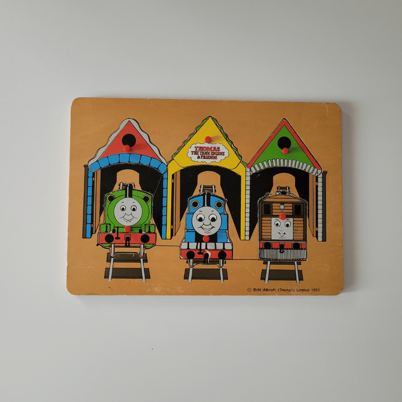 Vintage 'Thomas the Tank Engine' toy puzzle with three trains in different colored houses on a beige background.