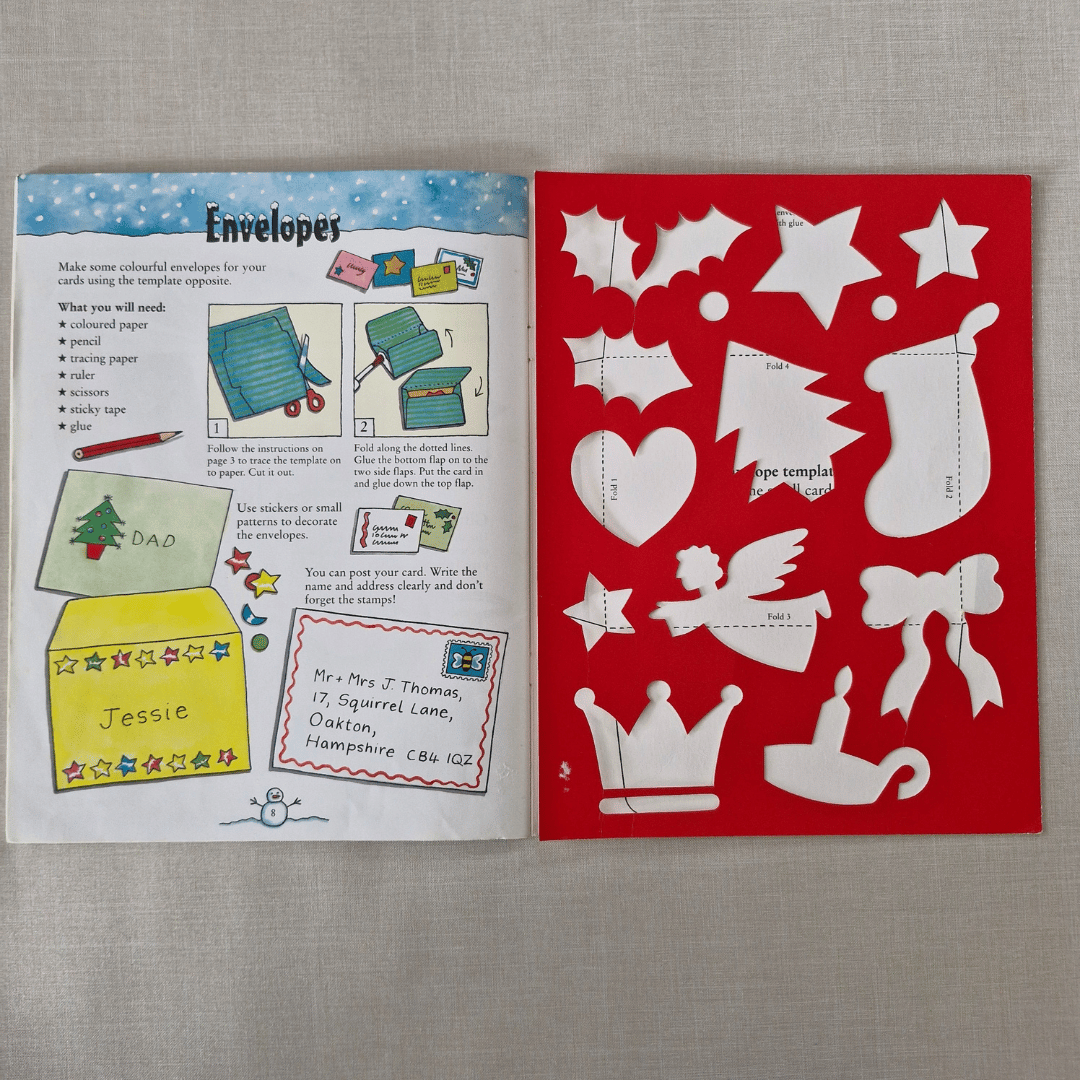 Open book with envelope template and cut-out shapes on a grey background