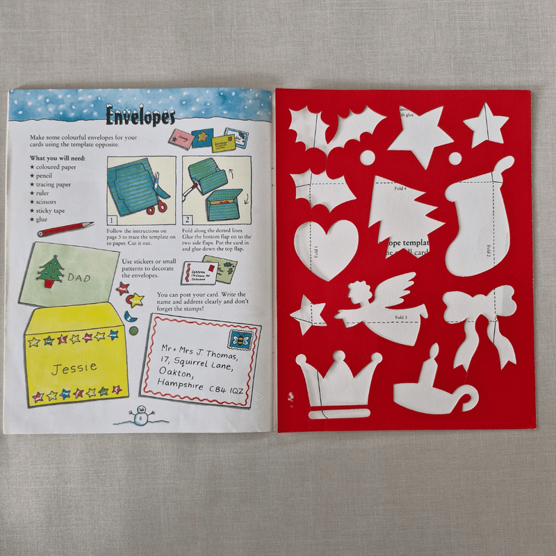 Open book with envelope template and cut-out shapes on a grey background