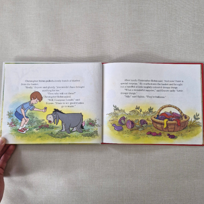Open book showing a page with Christopher Robin and Eeyore illustration and text on a gray surface.