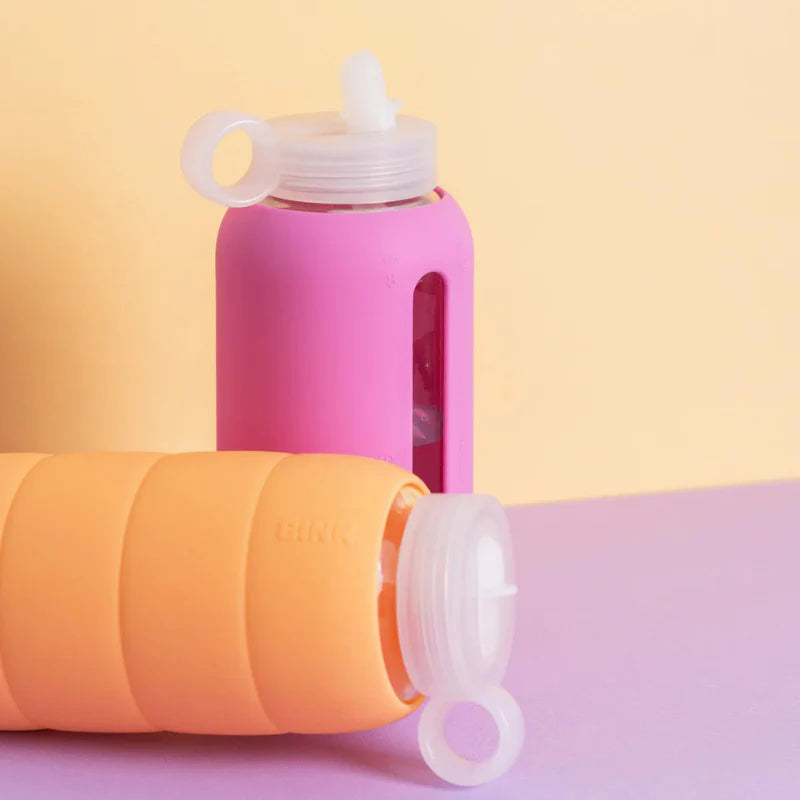 Pink and orange silicone water bottles with white lids on a pastel background