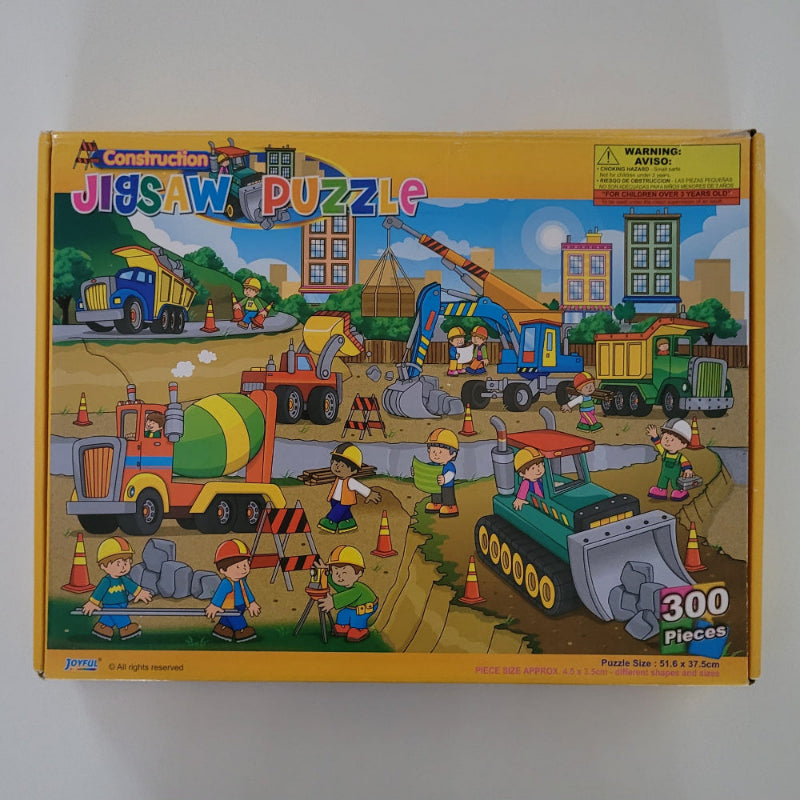 Construction-themed jigsaw puzzle box with colourful illustrations on a white background