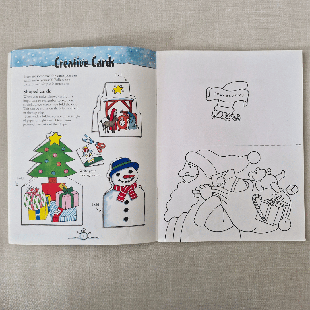 Open book with Christmas-themed colouring pages/cards and instructions on a textured surface
