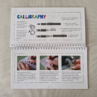 Open book with instructions on calligraphy and pen usage on a textured surface