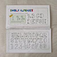 Open spiral-bound book with swirly alphabet and numbers on a textured surface