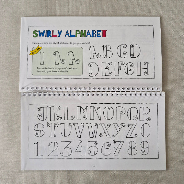 Open spiral-bound book with swirly alphabet and numbers on a textured surface