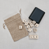 Black container, beige drawstring bag, and Scrabble tiles on a light grey background