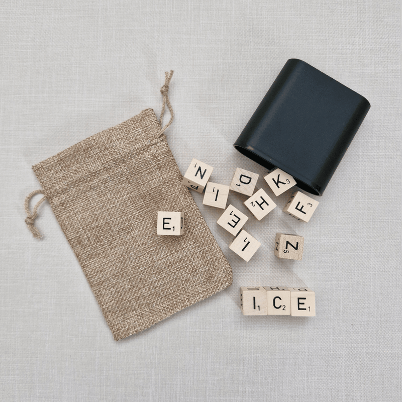 Black container, beige drawstring bag, and Scrabble tiles on a light grey background