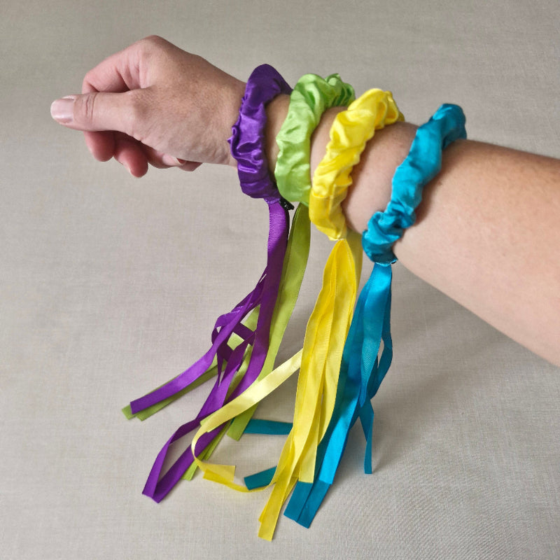 Colorful ribbon bracelets on a person's wrist against a neutral background