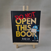 Book titled 'Do Not Open This Book' by Andy Lee on a stand with a grey background
