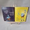 Open book with colourful illustrations of a blue creature on a grey background