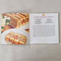 Open cookbook showing a recipe for 'Festive Tiramisu Terrine' on a textured surface.