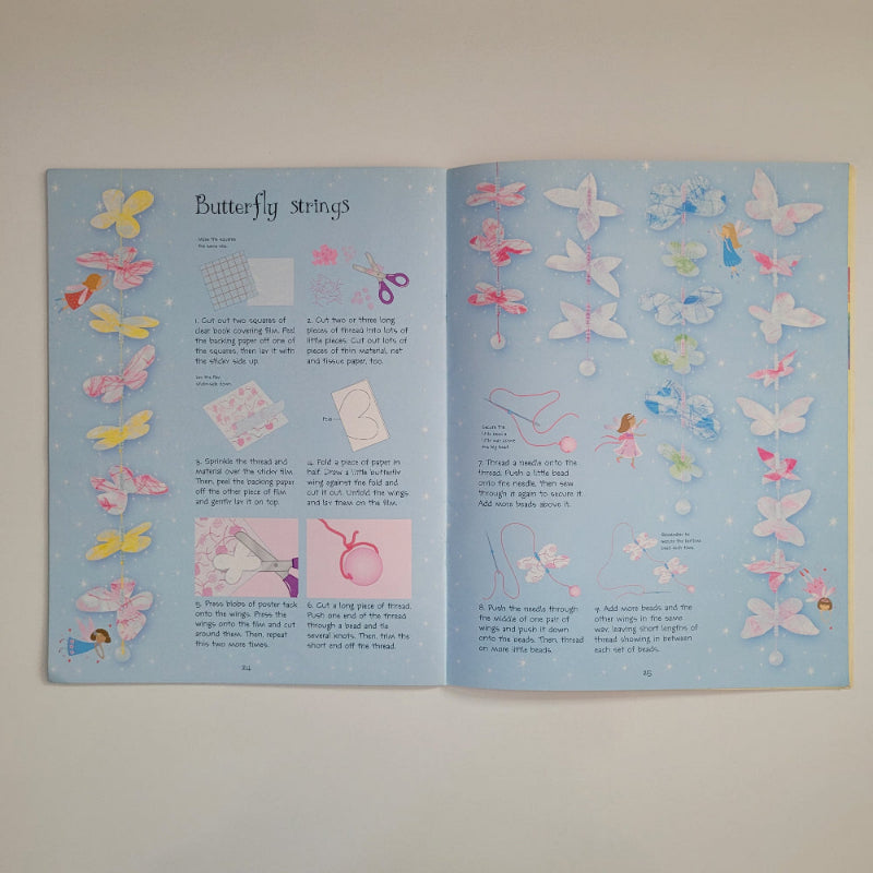 An open book on a light beige surface. The pages are pale blue and decorated with many pastel butterfly illustrations in pink, yellow, white, and blue, plus small step-by-step sewing or craft instructions and a title reading 'butterfly strings.
