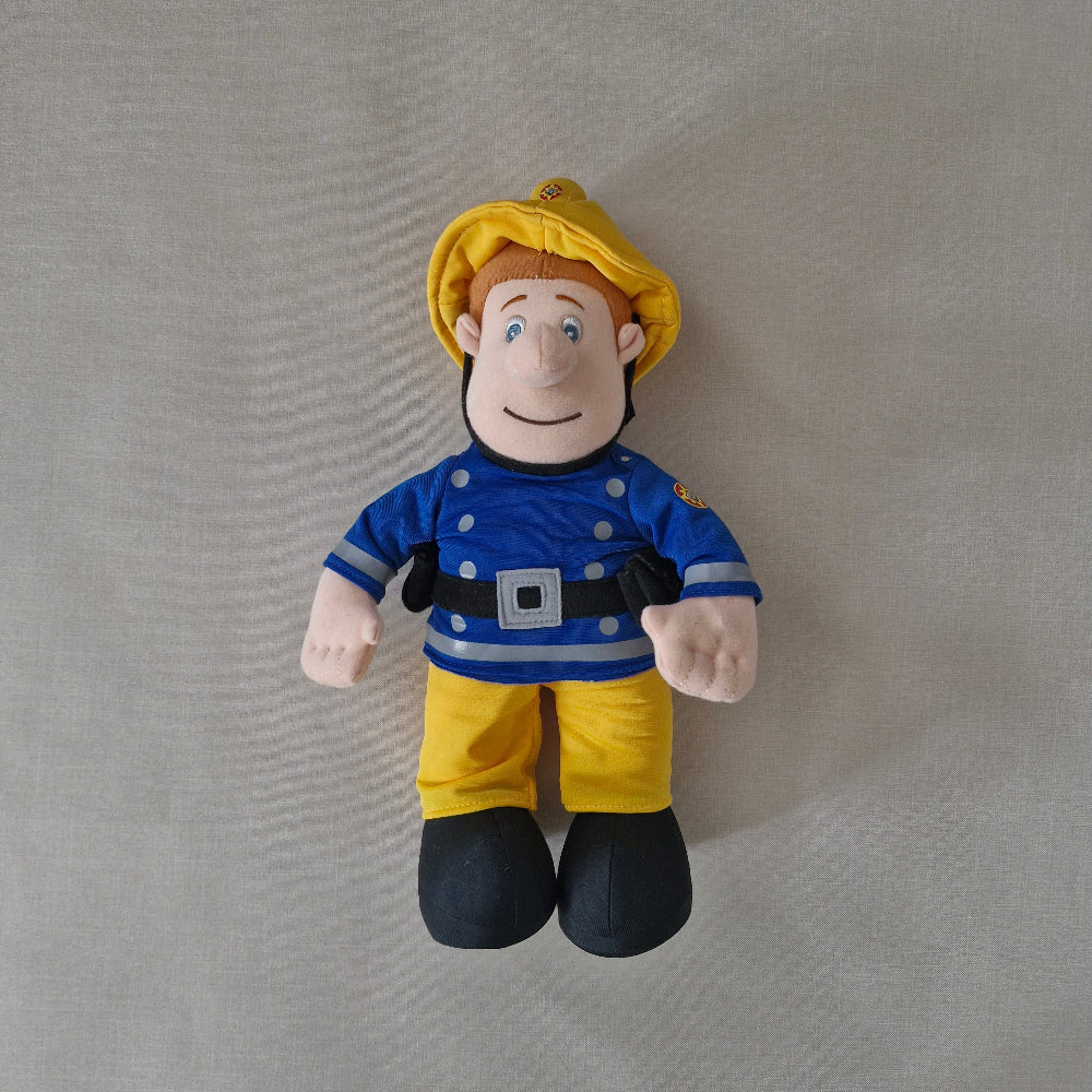 Plush toy figure of a character in a blue shirt and yellow pants on a grey background