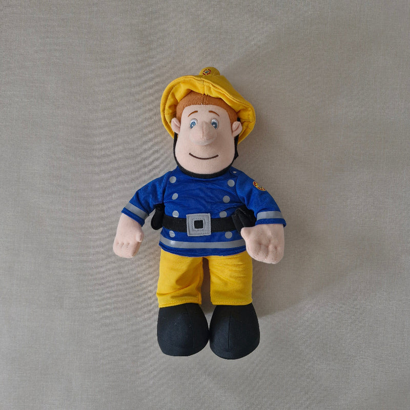 Plush toy figure of a character in a blue shirt and yellow pants on a grey background