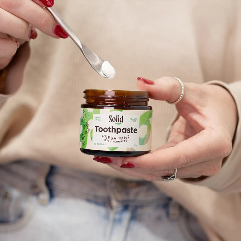 Person using a spoon to take Solid Toothpaste from a jar.