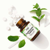 Bottle of toothpaste tablets with mint leaves on a white background