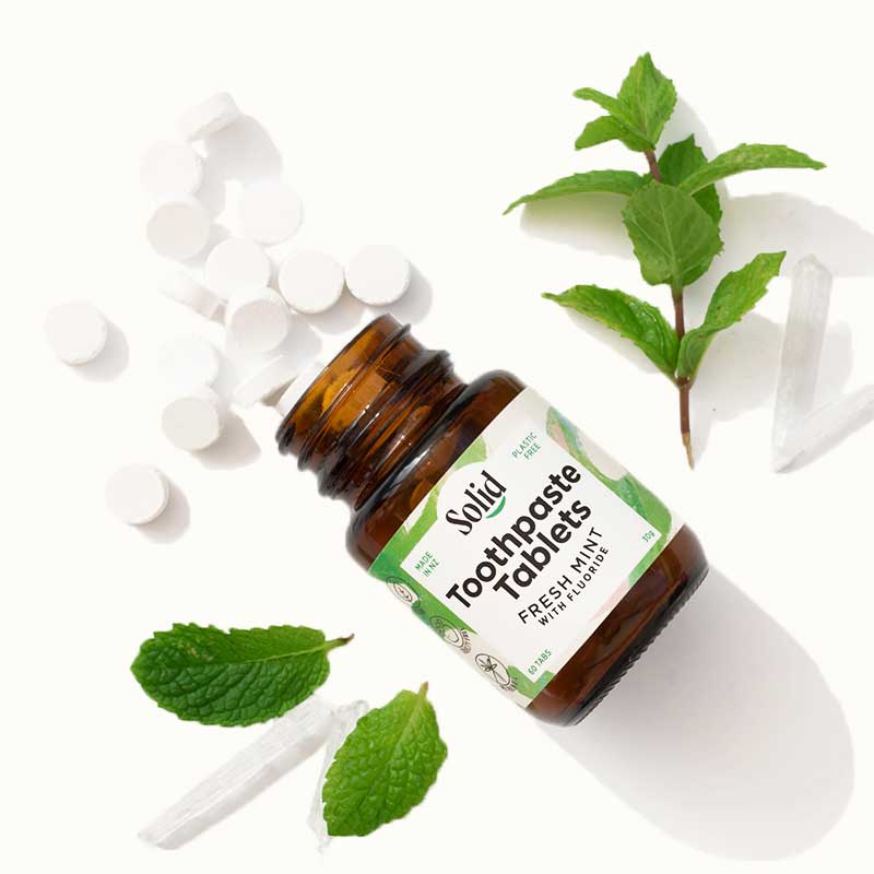Bottle of toothpaste tablets with mint leaves on a white background