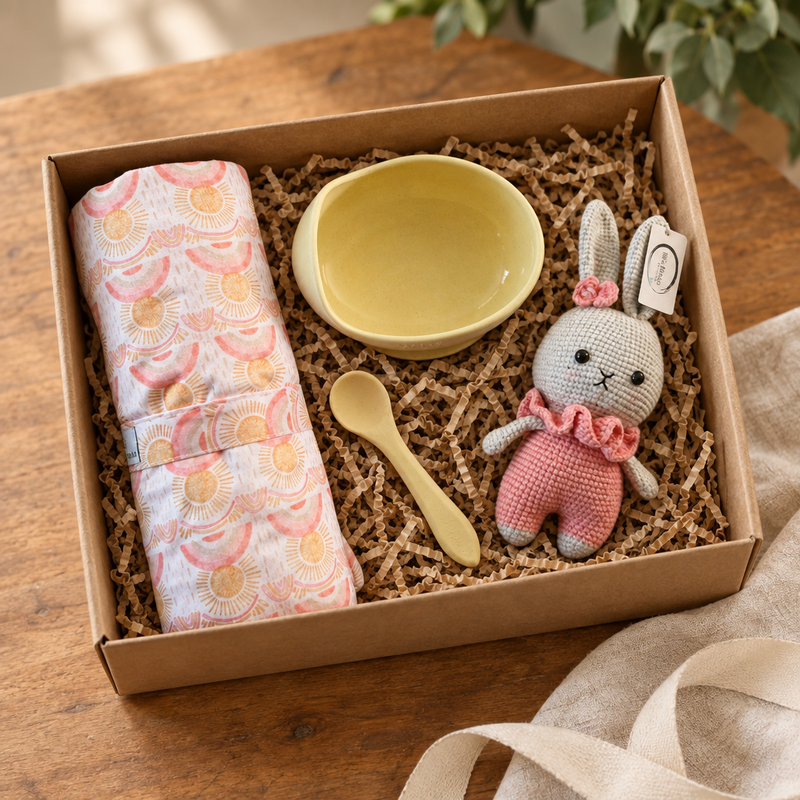 A set of baby shower gifts including a silicone lemonade bowl and spoon, a plush toy that looks like a bunny, an changing mat.