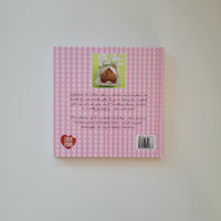 The back cover of a book with a pink and white gingham pattern, featuring a small photo of a heart-shaped sandwich, and handwritten text on a plain white background.