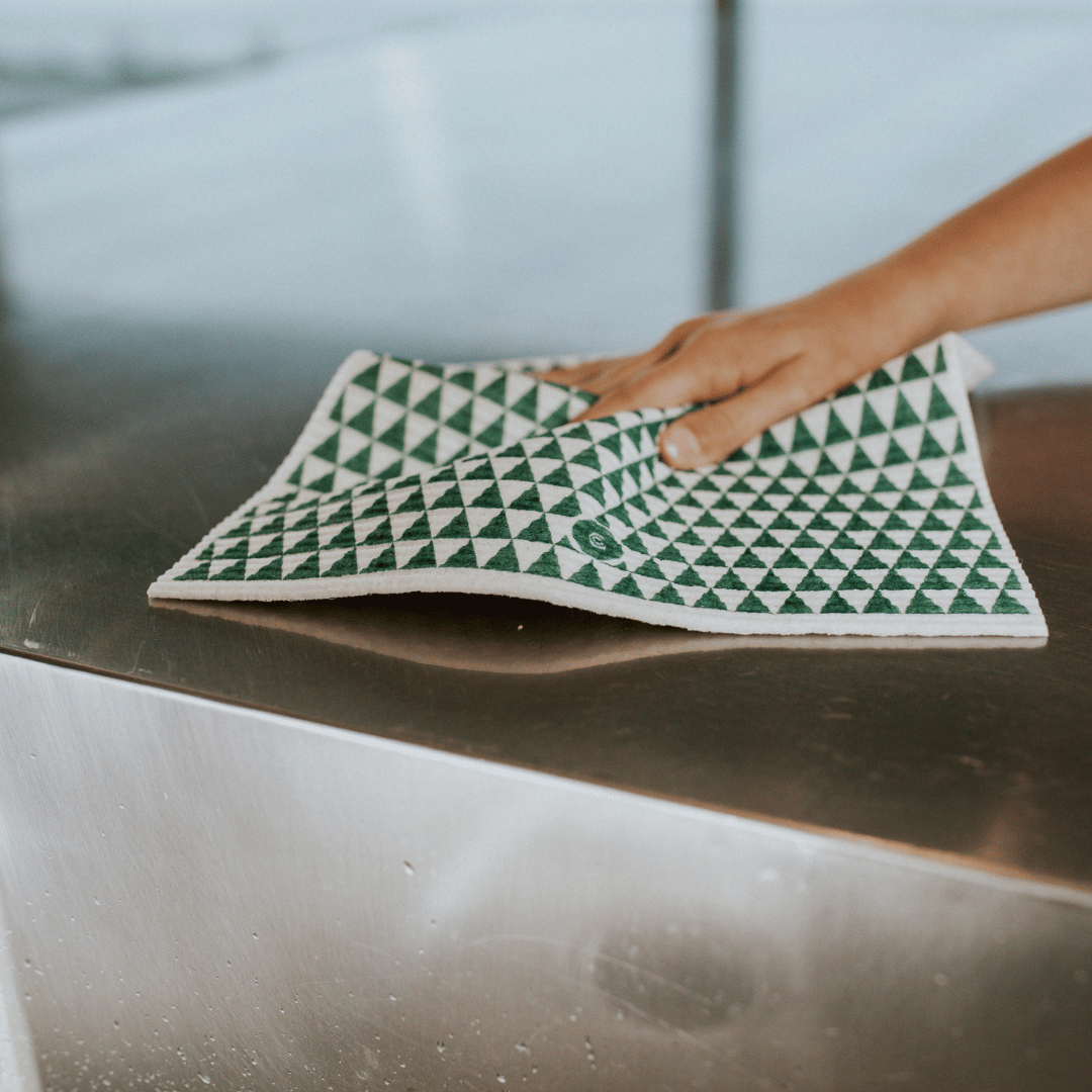 Person using a green and white patterned cloth on a metallic surface