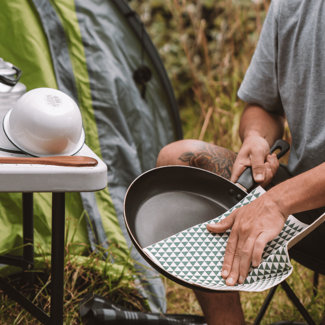 Person holding a frying pan and drying it with an eco cloth in an outdoor setting