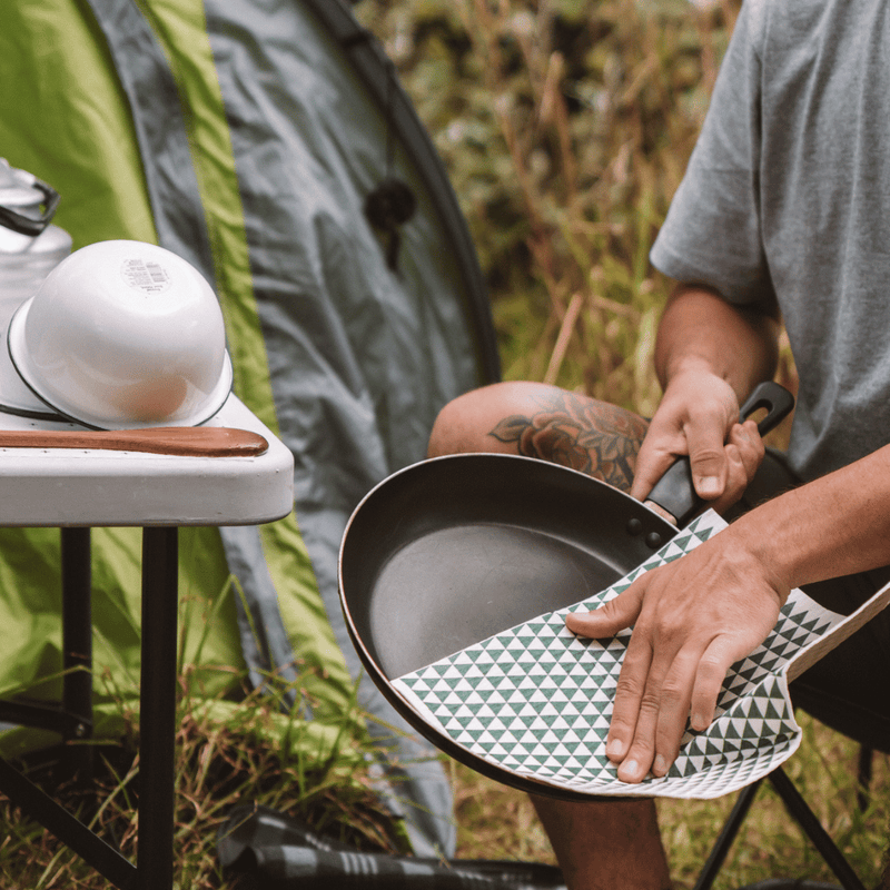 Person holding a frying pan and drying it with an eco cloth in an outdoor setting