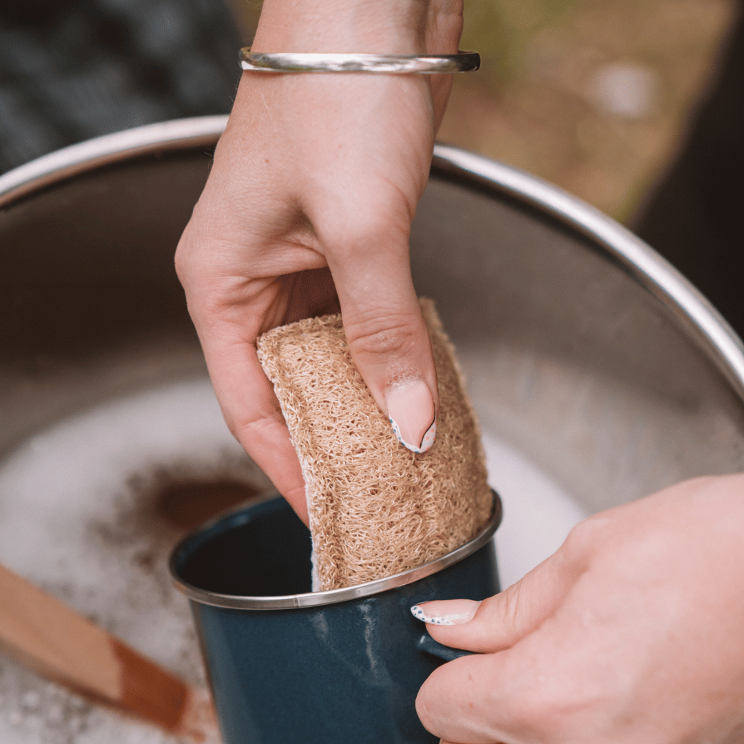 Person cleaning a blue mug with an eco scrub sponge in a sink